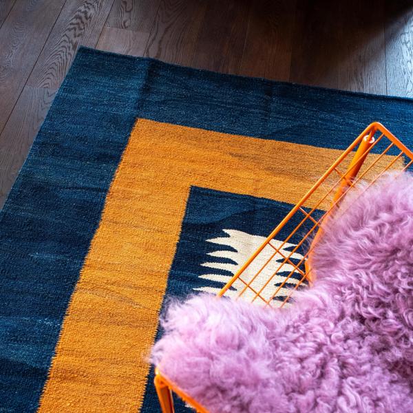 Close-up of a Gabbeh rug with a geometric pattern in blue and yellow, orange chair un